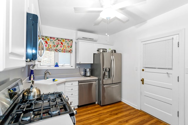 kitchen with an AC wall unit, stainless steel appliances, wood-type flooring, and white cabinets