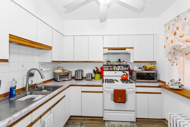 kitchen with white cabinets, white gas stove, sink, and radiator