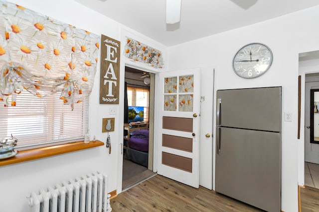 kitchen with radiator heating unit, a healthy amount of sunlight, wood-type flooring, and stainless steel refrigerator