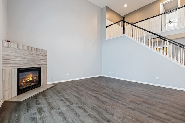 unfurnished living room with a tiled fireplace, wood-type flooring, and a high ceiling