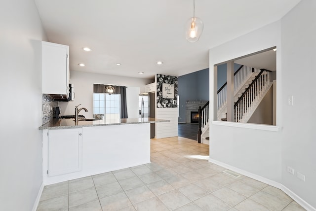 kitchen featuring light stone countertops, sink, white cabinetry, and decorative light fixtures