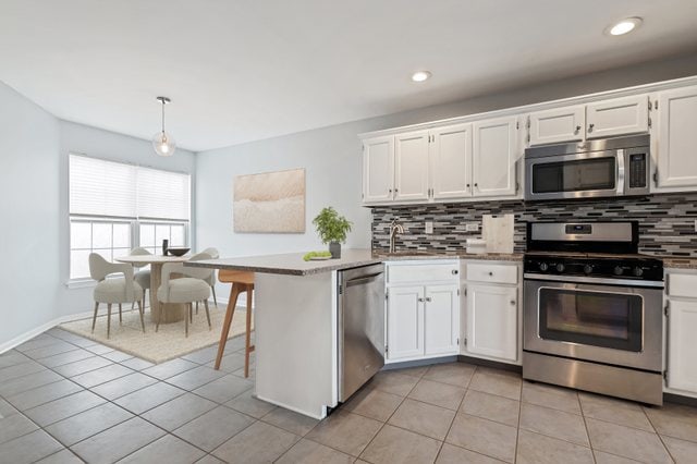 kitchen with kitchen peninsula, stainless steel appliances, backsplash, pendant lighting, and white cabinetry