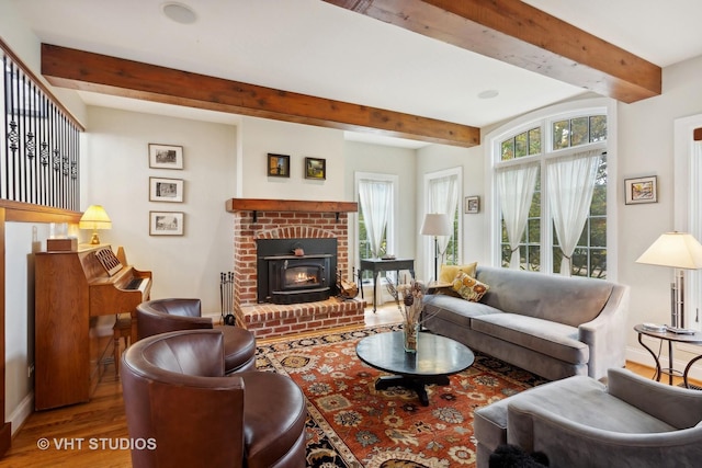 living room featuring beamed ceiling, plenty of natural light, wood-type flooring, and a brick fireplace