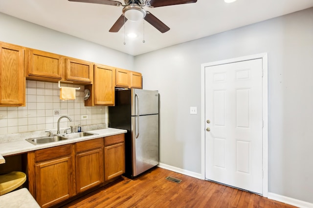 kitchen with dark wood-type flooring, sink, stainless steel refrigerator, backsplash, and ceiling fan