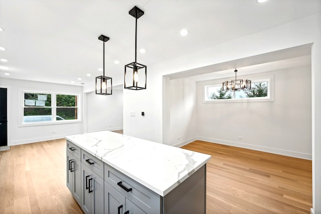 kitchen with light stone counters, gray cabinetry, decorative light fixtures, light hardwood / wood-style floors, and a kitchen island