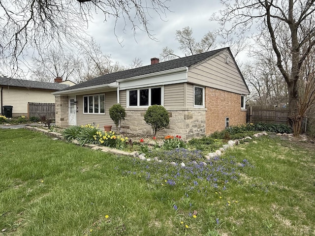 view of side of home with fence, stone siding, a chimney, and a yard