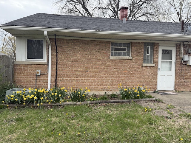 view of home's exterior with brick siding, a shingled roof, a chimney, and fence