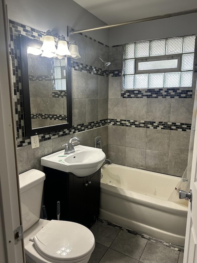 bathroom with tile patterned floors, bathing tub / shower combination, toilet, vanity, and tile walls