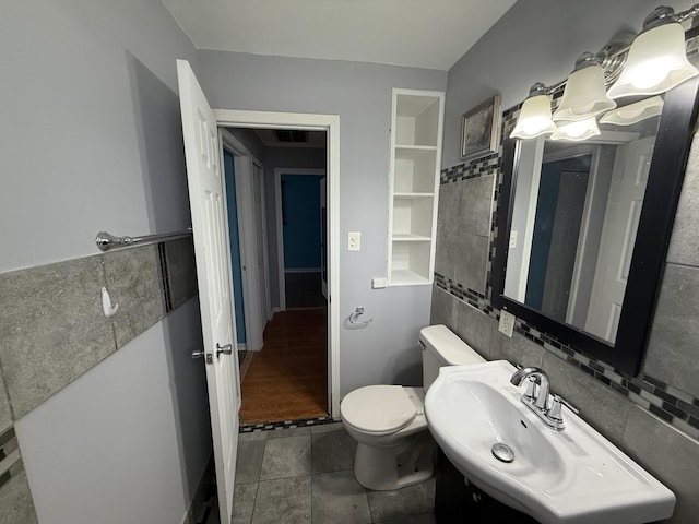 half bath featuring tile walls, built in features, a sink, and toilet