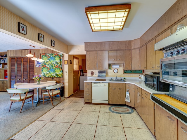 kitchen with hanging light fixtures, wood walls, sink, dishwasher, and light colored carpet