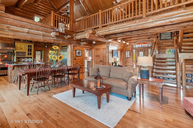 living room with light hardwood / wood-style floors, beamed ceiling, high vaulted ceiling, wood ceiling, and log walls