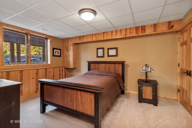 carpeted bedroom featuring wooden walls and a drop ceiling