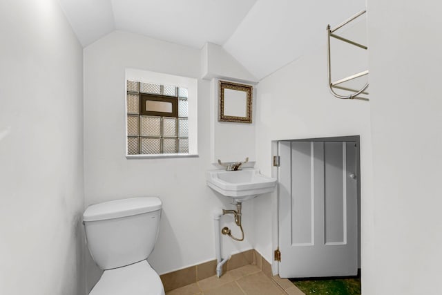 bathroom featuring toilet, vaulted ceiling, a sink, tile patterned flooring, and baseboards