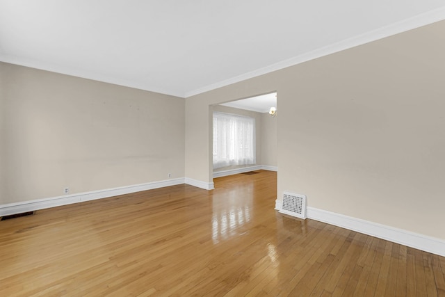 empty room featuring crown molding, wood-type flooring, visible vents, and baseboards