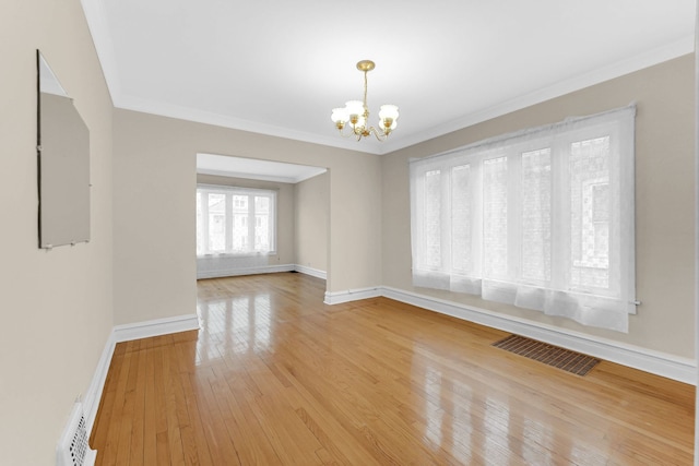 spare room featuring visible vents, an inviting chandelier, light wood-style floors, ornamental molding, and baseboards