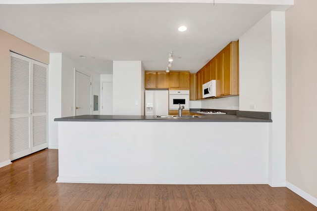 kitchen with light wood-type flooring, white appliances, kitchen peninsula, and sink