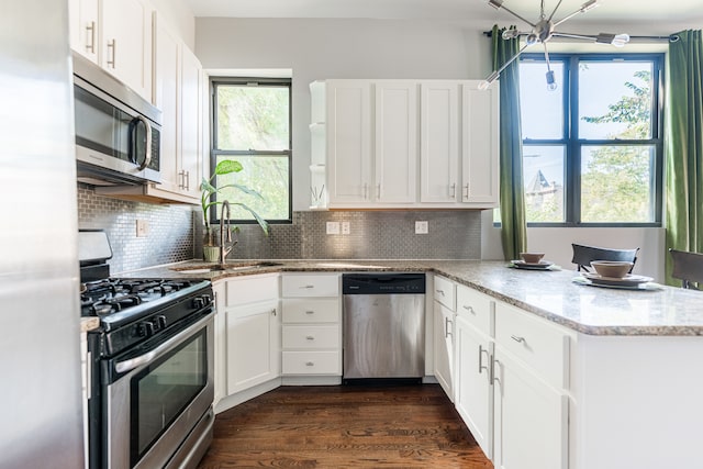 kitchen with white cabinets, kitchen peninsula, appliances with stainless steel finishes, and dark hardwood / wood-style flooring