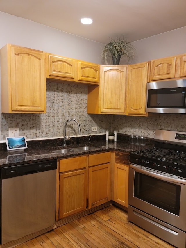 kitchen featuring backsplash, dark stone counters, sink, light hardwood / wood-style flooring, and stainless steel appliances