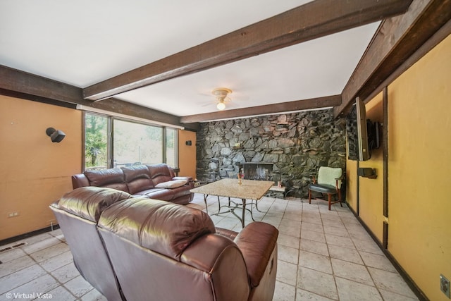 living room with ceiling fan, a stone fireplace, and beamed ceiling