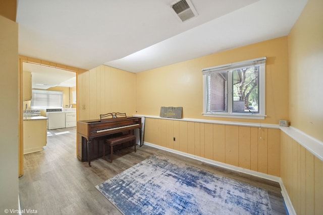 misc room with light wood-type flooring, wood walls, and washing machine and clothes dryer