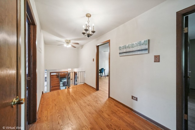 unfurnished living room with ceiling fan with notable chandelier and light hardwood / wood-style flooring