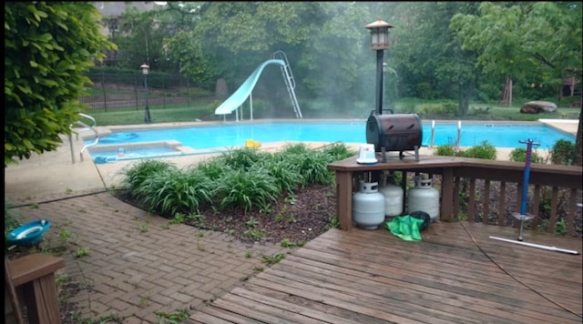 view of pool with a patio area, a water slide, a wooden deck, and a grill