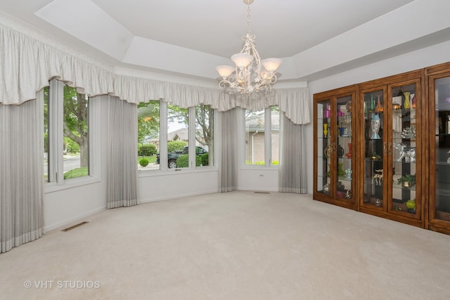 empty room featuring a notable chandelier, a tray ceiling, and light carpet