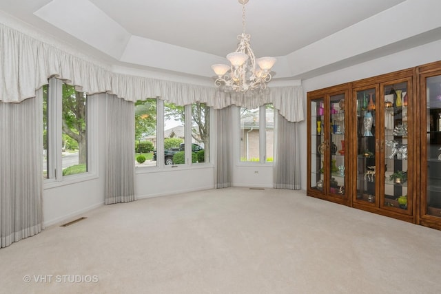 unfurnished dining area featuring visible vents, a chandelier, carpet flooring, and a raised ceiling