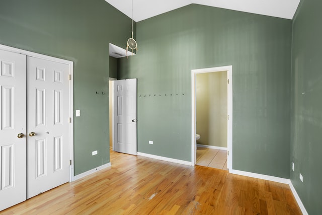 unfurnished bedroom featuring light wood-type flooring, connected bathroom, high vaulted ceiling, and a closet