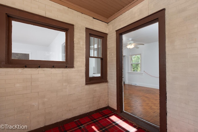 entryway featuring dark parquet floors, ceiling fan, and brick wall