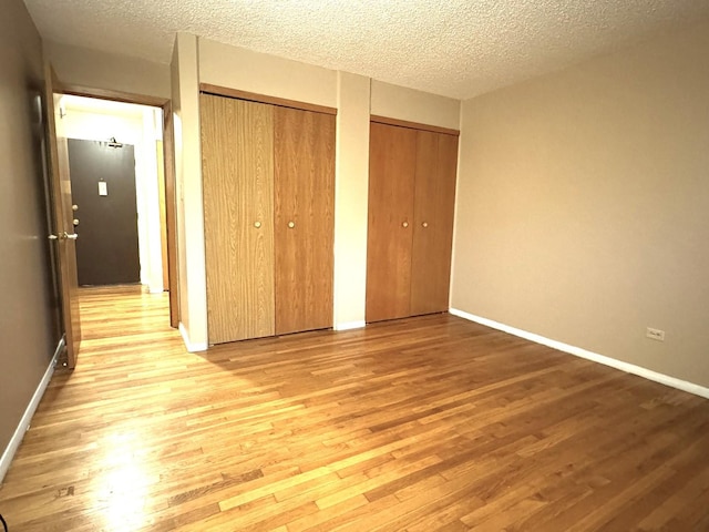 unfurnished bedroom featuring a textured ceiling, light hardwood / wood-style flooring, and two closets