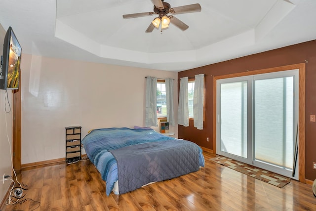 bedroom featuring ceiling fan, hardwood / wood-style flooring, a raised ceiling, and access to outside