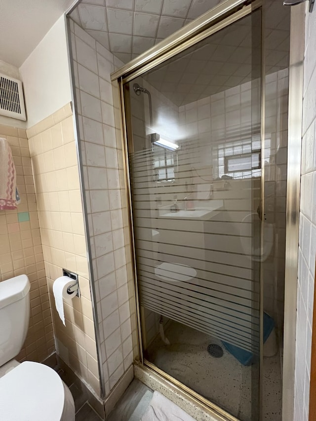 bathroom with tile walls, a shower with door, and toilet