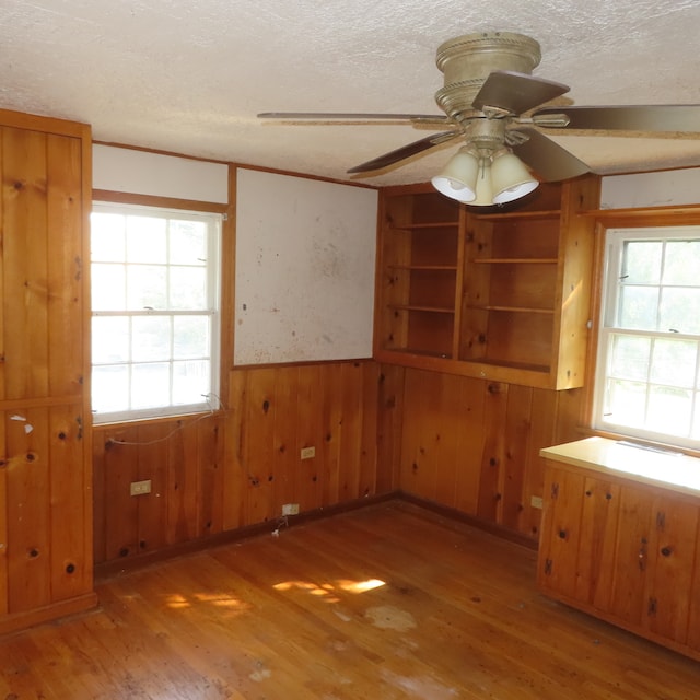 unfurnished room featuring a textured ceiling, light hardwood / wood-style floors, wood walls, and ceiling fan