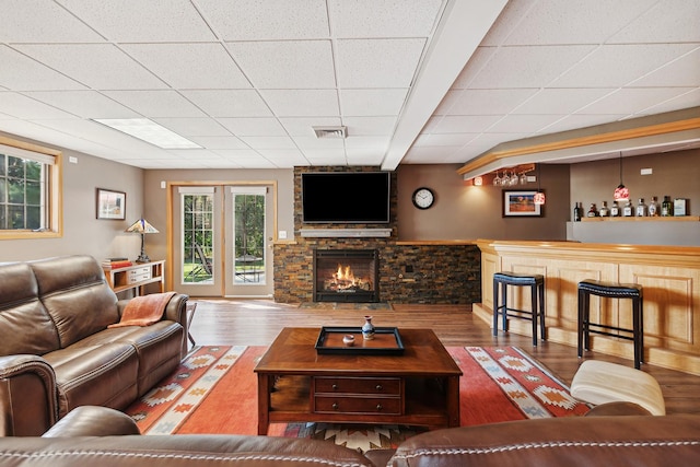 living room featuring a stone fireplace, hardwood / wood-style floors, and a drop ceiling