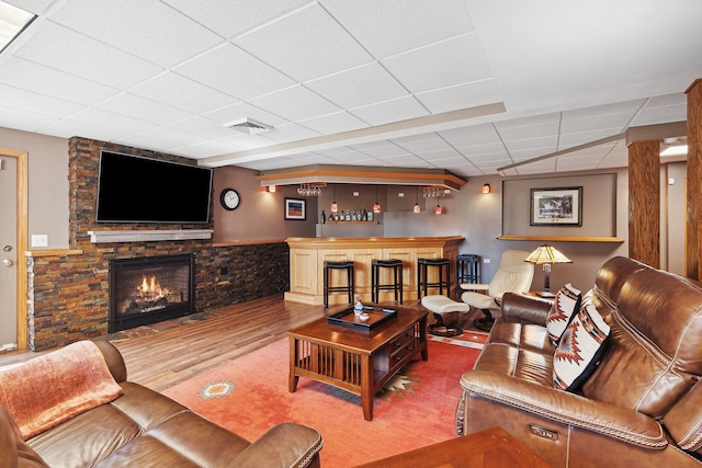 living room with a paneled ceiling, hardwood / wood-style floors, a fireplace, and bar area