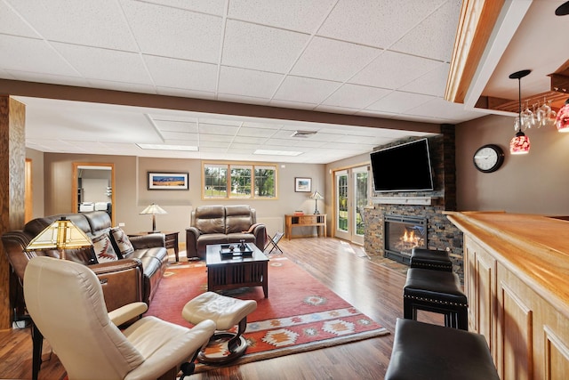 living room featuring hardwood / wood-style flooring, a stone fireplace, and a drop ceiling