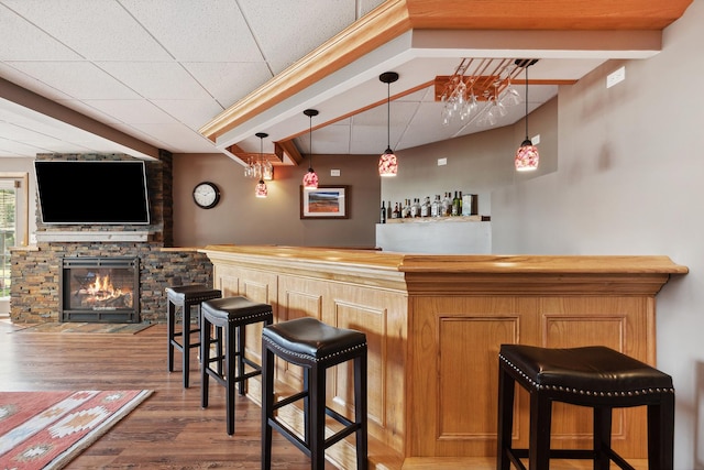 bar featuring pendant lighting, a stone fireplace, dark wood-type flooring, and beam ceiling