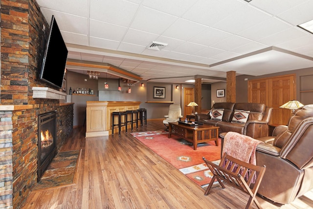 living room featuring hardwood / wood-style flooring, a paneled ceiling, a fireplace, and bar