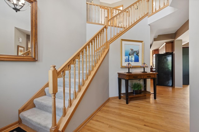 staircase featuring a chandelier, wood-type flooring, and a high ceiling