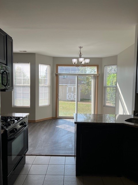 kitchen featuring light tile patterned floors, baseboards, black range with gas stovetop, an inviting chandelier, and dark cabinetry