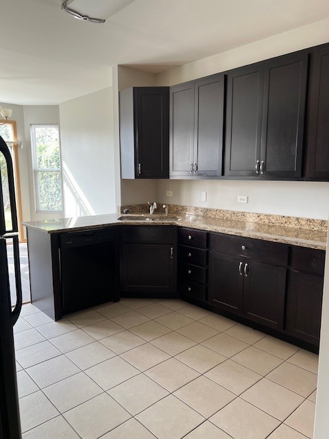 kitchen featuring light stone countertops, a sink, dark cabinetry, light tile patterned floors, and black appliances