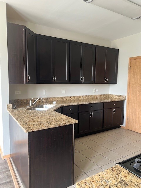kitchen with light tile patterned flooring, light stone countertops, a sink, dark cabinets, and a peninsula