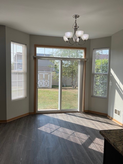 unfurnished dining area featuring dark wood-style flooring, baseboards, a notable chandelier, and plenty of natural light