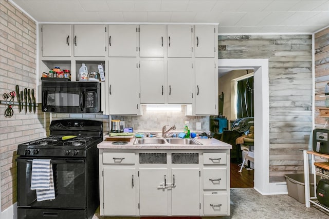 kitchen featuring black appliances, brick wall, white cabinetry, and sink