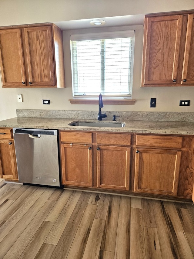 kitchen with light stone countertops, light hardwood / wood-style floors, sink, and stainless steel dishwasher