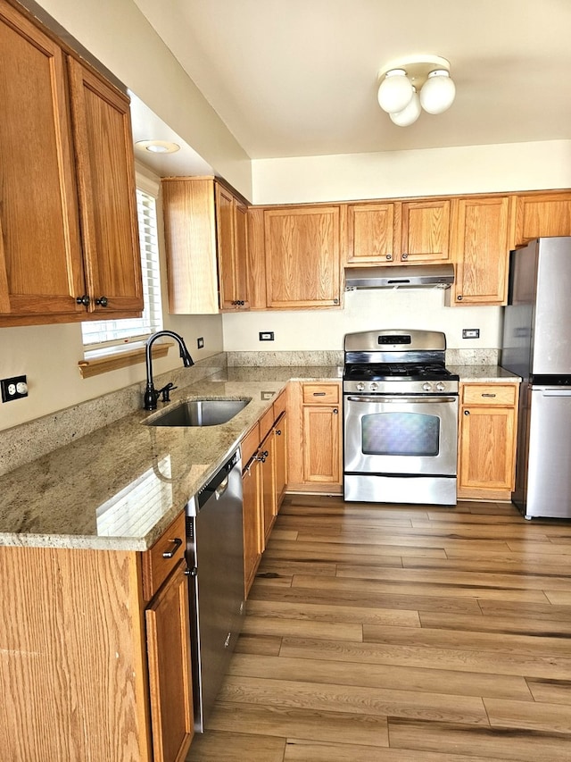 kitchen featuring appliances with stainless steel finishes, light stone counters, sink, and light hardwood / wood-style floors