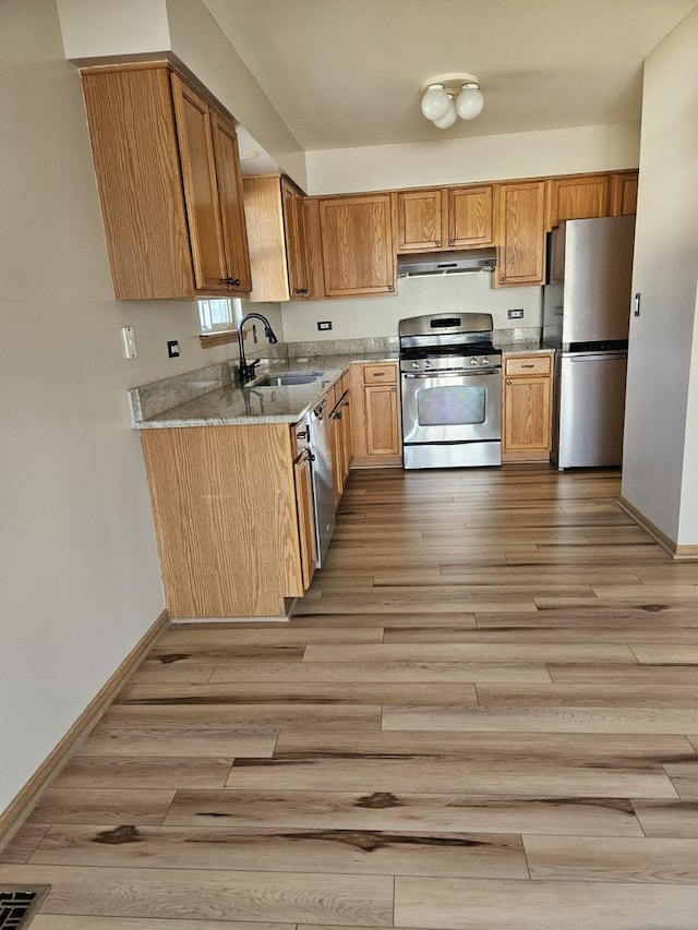 kitchen with light hardwood / wood-style floors, appliances with stainless steel finishes, sink, and light stone countertops