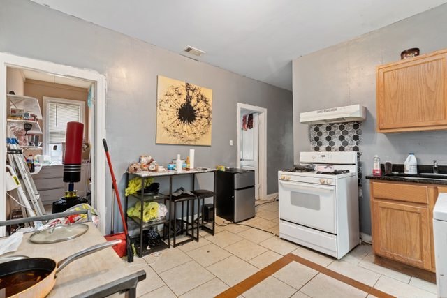 kitchen featuring stainless steel refrigerator, light tile patterned floors, white gas range, sink, and extractor fan