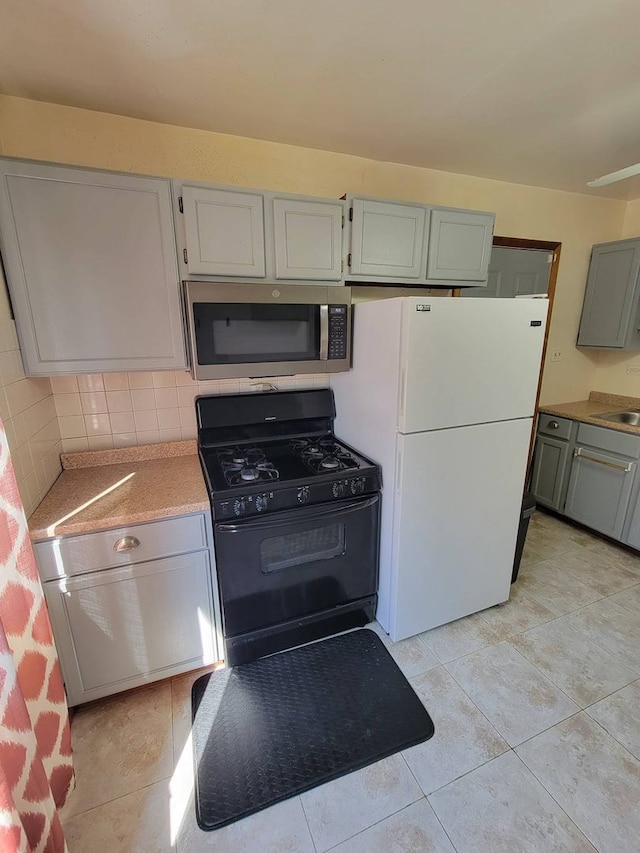 kitchen with gray cabinetry, tasteful backsplash, white refrigerator, light tile patterned floors, and gas stove